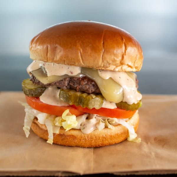 A Buns Burgers cheeseburger with special sauce, pickles, tomato, and lettuce on a bun.