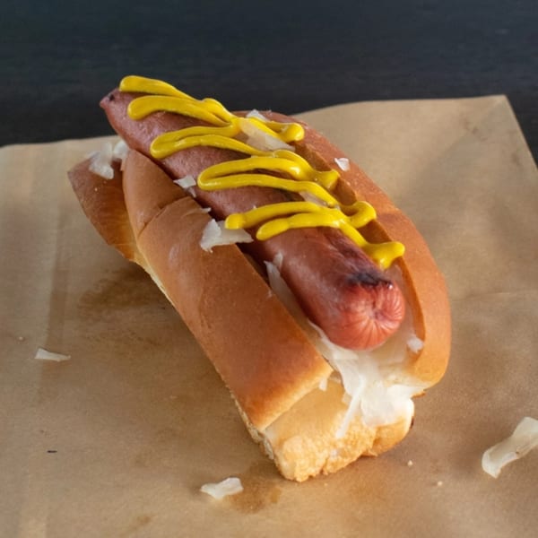 Grilled hot dog with mustard and onions in a bun, served on brown paper.