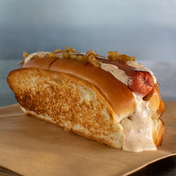 A hot dog in a toasted bun, topped with caramelized onions and a creamy sauce.